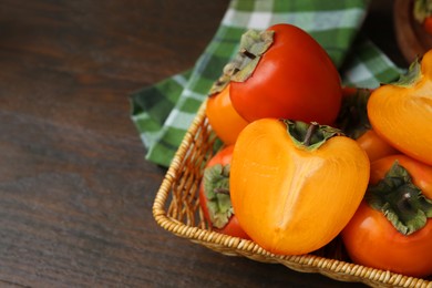 Photo of Whole and cut juicy persimmons in wicker basket on wooden table, closeup. Space for text