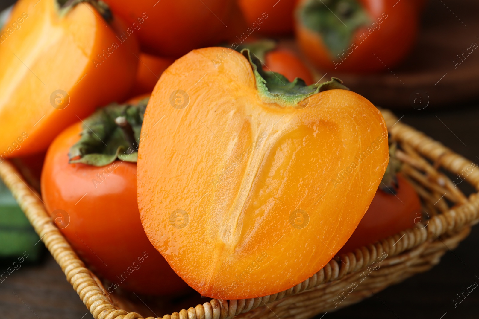 Photo of Whole and cut fresh persimmons in wicker basket on table, closeup