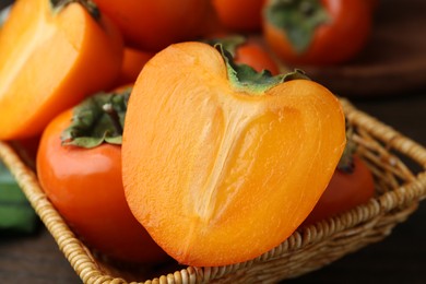 Whole and cut fresh persimmons in wicker basket on table, closeup