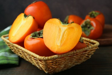 Photo of Whole and cut juicy persimmons in wicker basket on wooden table, closeup