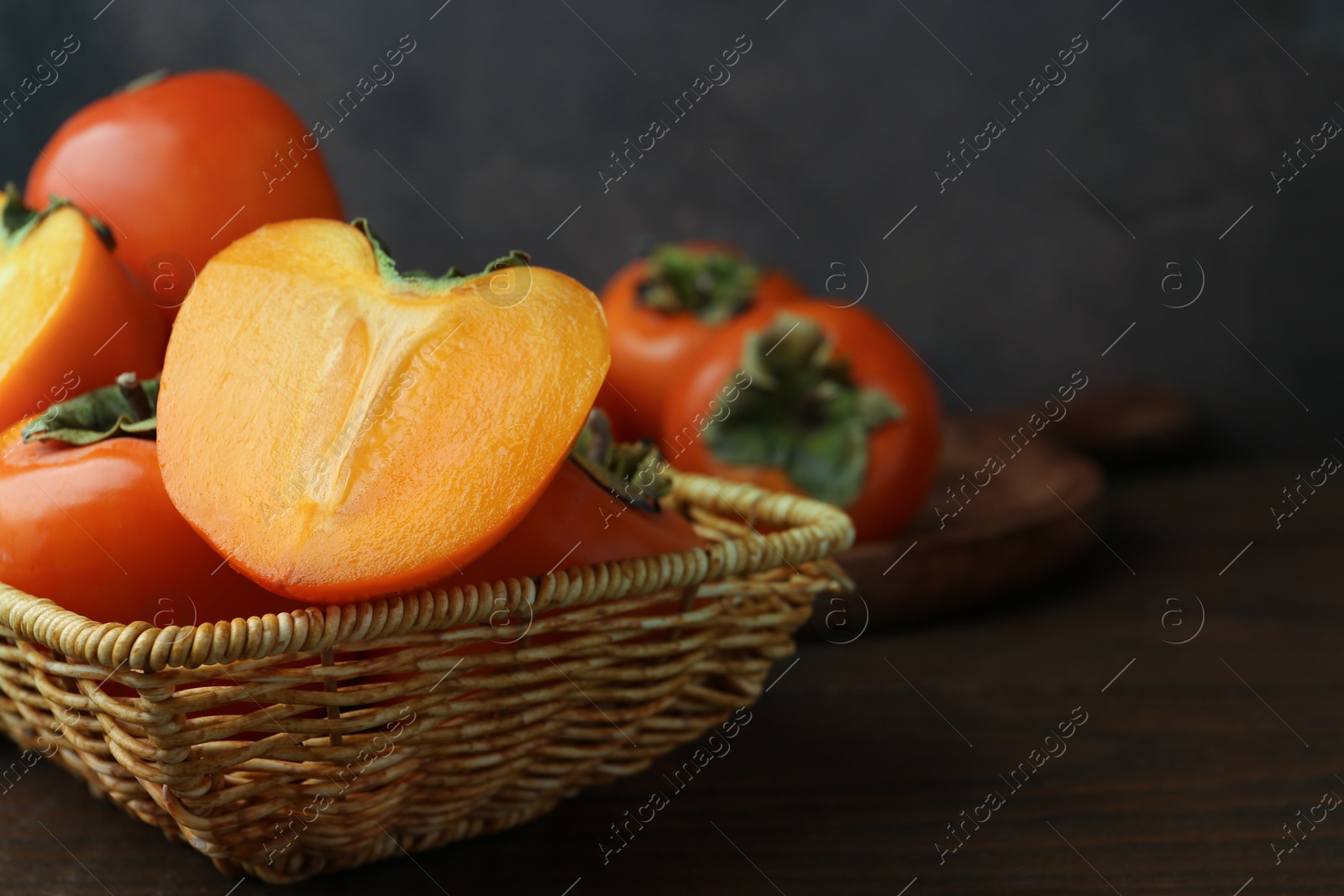 Photo of Delicious fresh juicy persimmons in wicker basket on wooden table, closeup. Space for text