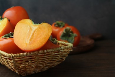 Photo of Delicious fresh juicy persimmons in wicker basket on wooden table, closeup. Space for text