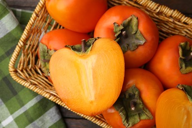 Photo of Whole and cut fresh persimmons in wicker basket on wooden table, top view