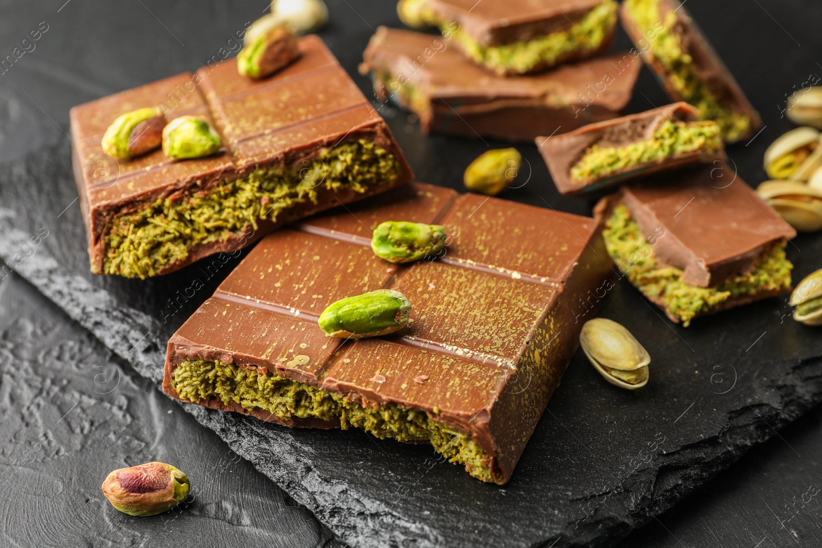 Photo of Pieces of Dubai chocolate bars with pistachios and knafeh on grey table, closeup