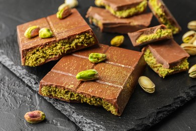 Photo of Pieces of Dubai chocolate bars with pistachios and knafeh on grey table, closeup