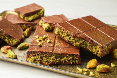 Photo of Pieces of Dubai chocolate bars with pistachios and knafeh on white table, closeup