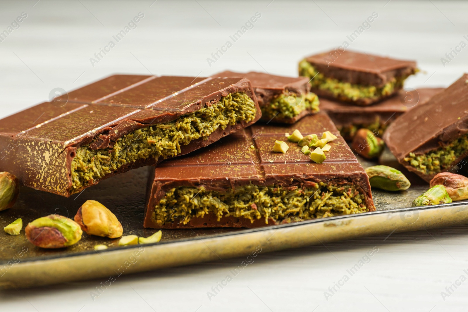 Photo of Pieces of Dubai chocolate bars with pistachios and knafeh on white table, closeup