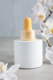 Photo of Bottle of skin care product and orchid flowers on gray textured surface