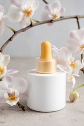 Photo of Bottle of skin care product and orchid flowers on gray textured surface