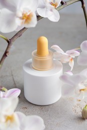 Photo of Bottle of skin care product and orchid flowers on gray textured surface