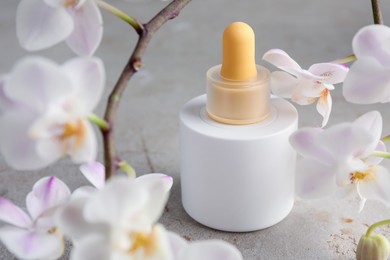 Photo of Bottle of skin care product and orchid flowers on gray textured surface, closeup