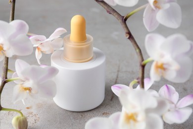 Photo of Bottle of skin care product and orchid flowers on gray textured surface, closeup