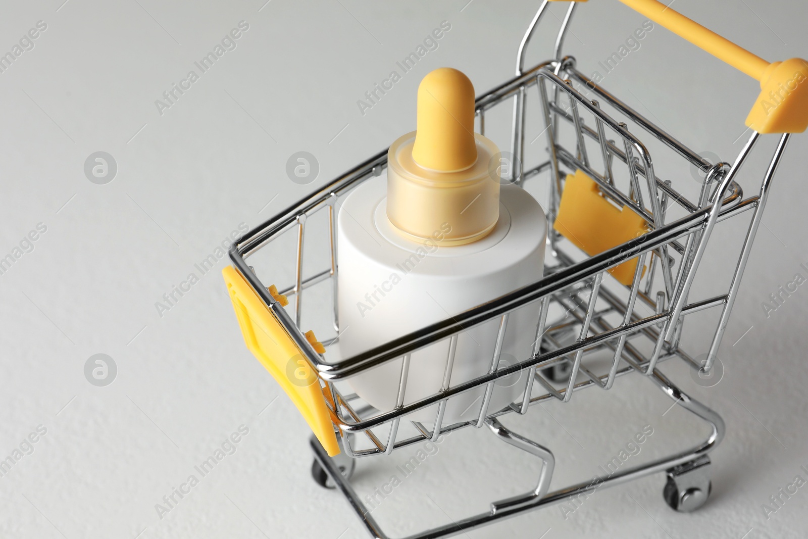 Photo of Bottle of skin care product in small shopping cart on light background, closeup. Space for text