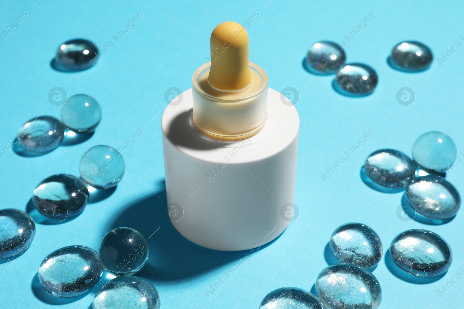 Photo of Bottle of skin care product and transparent decorative stones on light blue background