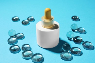 Photo of Bottle of skin care product and transparent decorative stones on light blue background