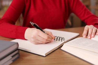 Photo of Girl taking notes at wooden desk in public library, closeup