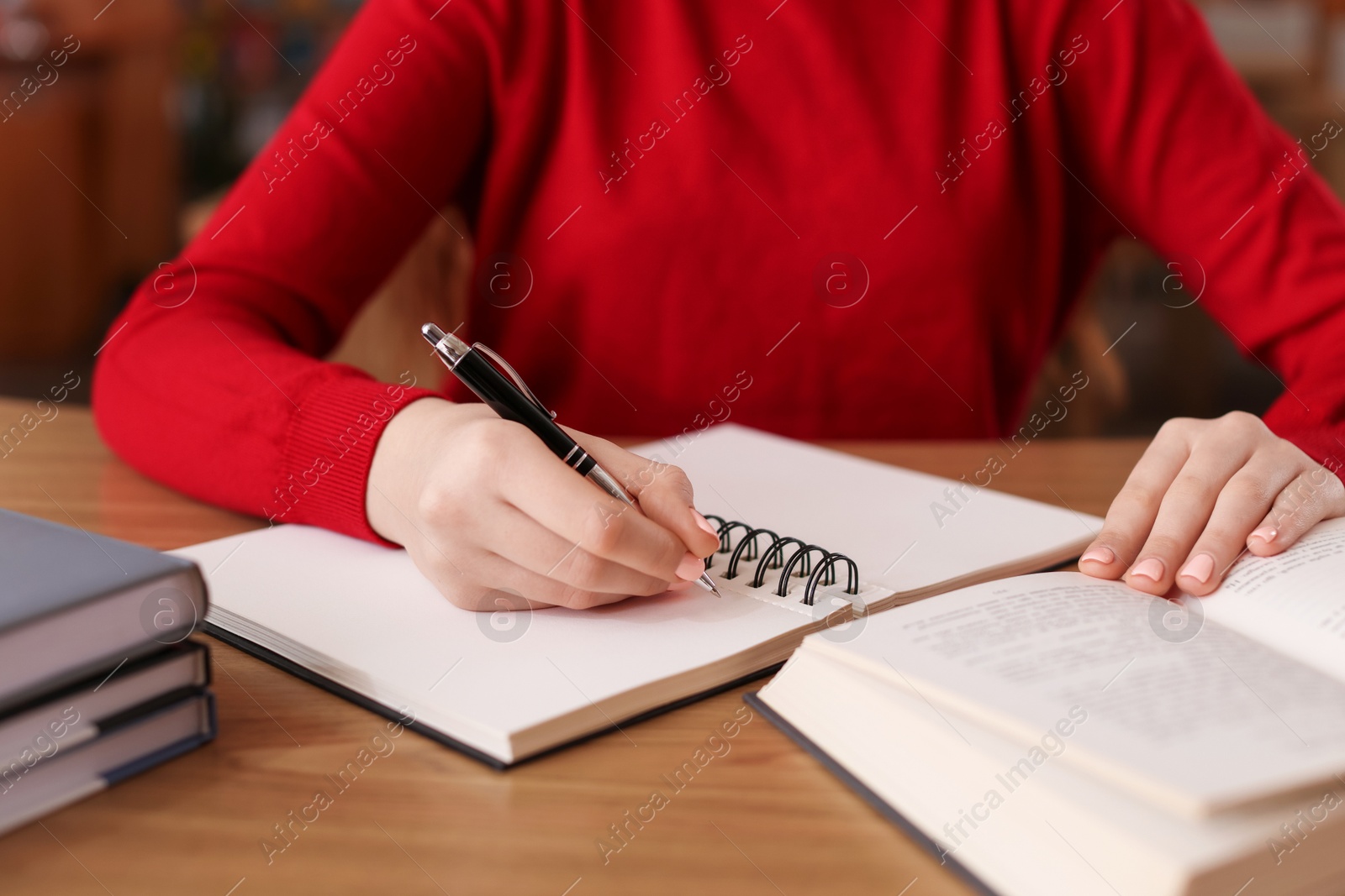 Photo of Girl taking notes at wooden desk in public library, closeup