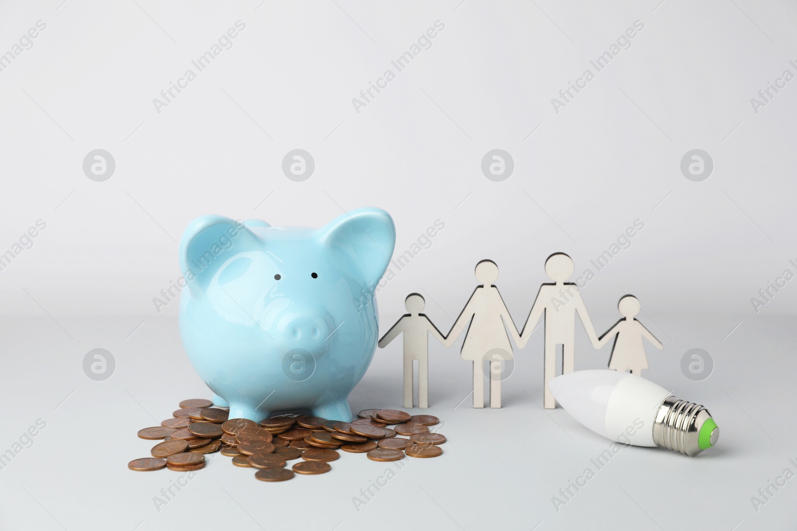 Photo of Piggy bank, coins, figure of family and light bulb on grey background. Energy saving concept