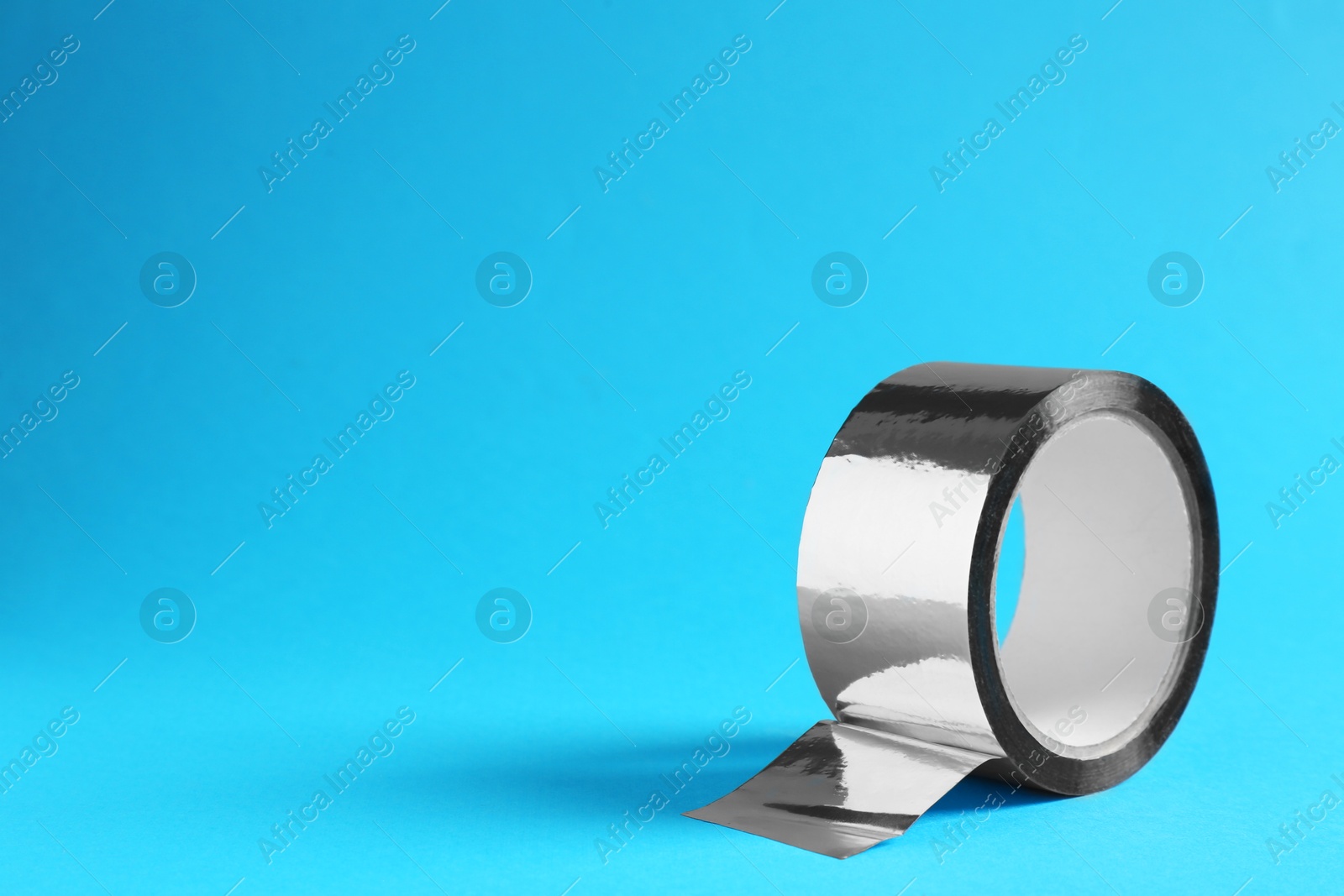 Roll of silver adhesive tape on light blue background, space for text Photo of Roll of silver adhesive tape on light blue background, space for text