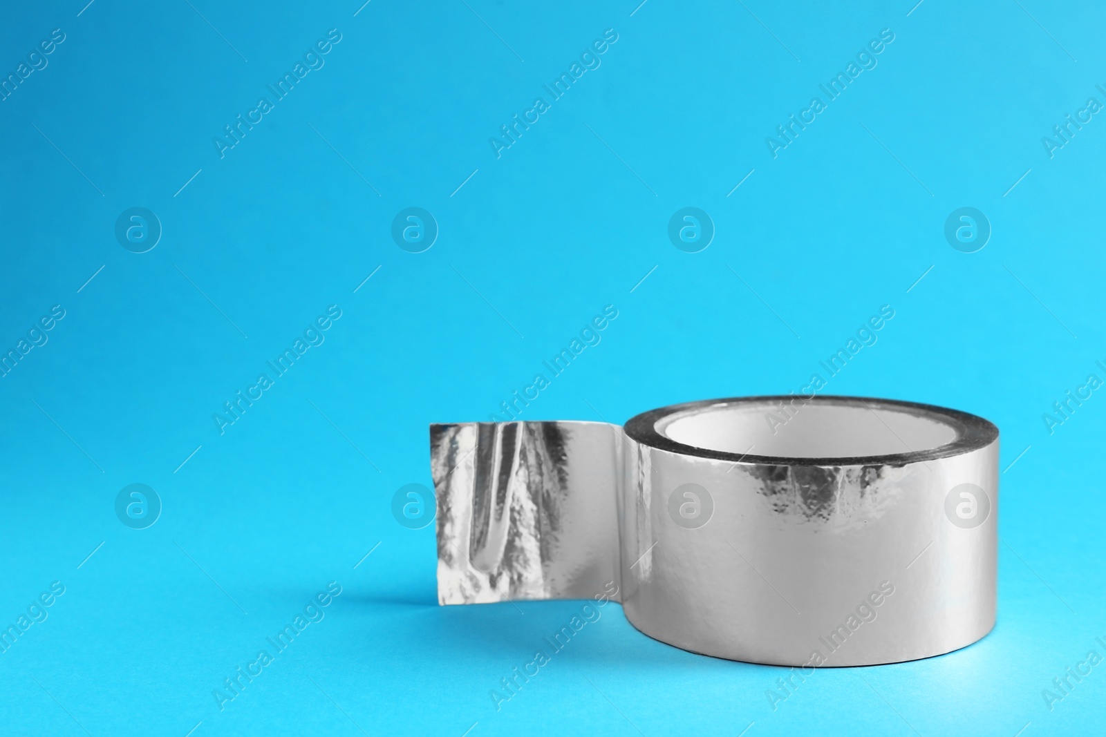 Photo of Roll of silver adhesive tape on light blue background, space for text