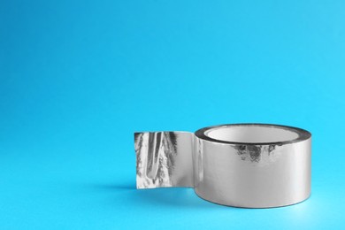 Photo of Roll of silver adhesive tape on light blue background, space for text