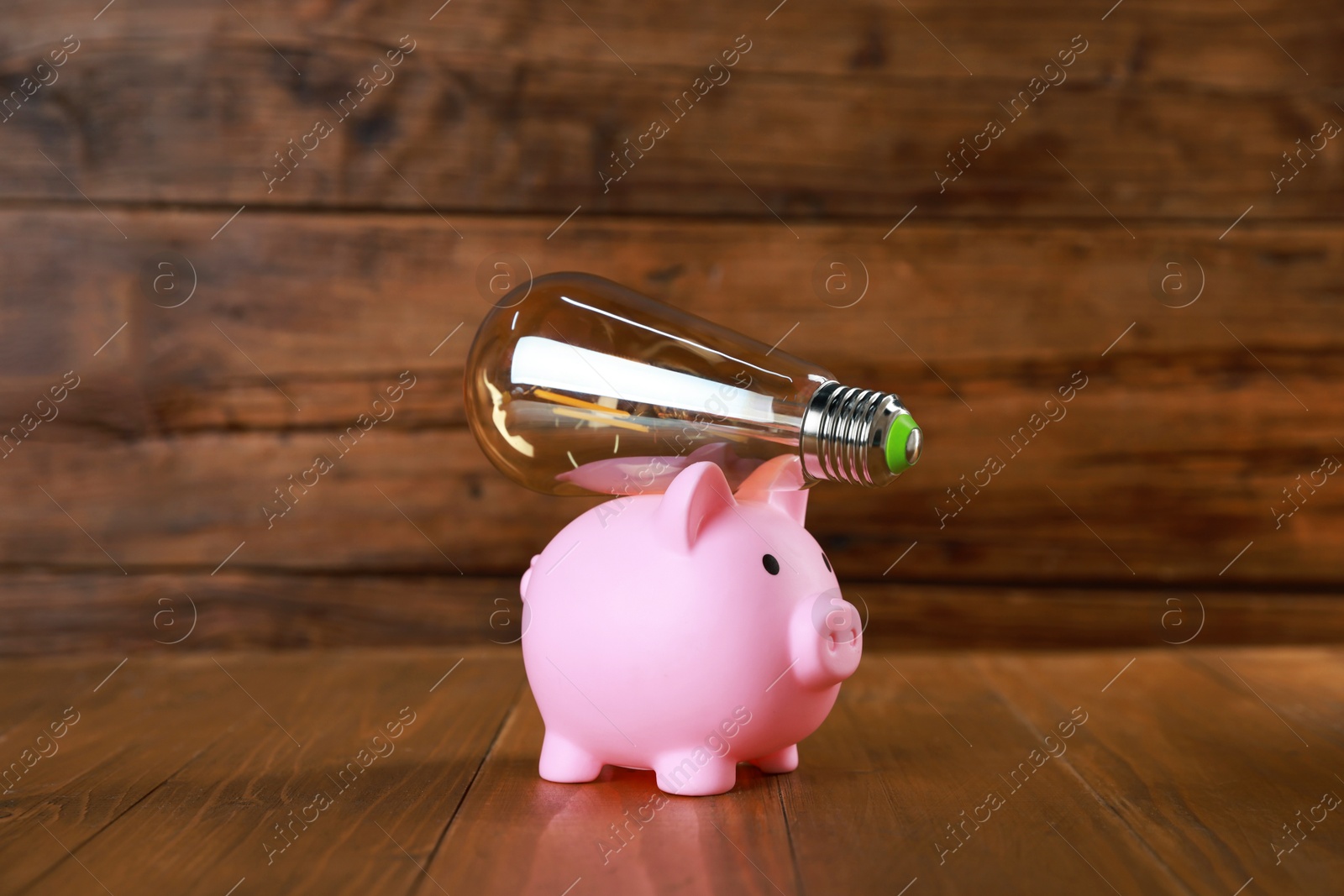 Photo of Piggy bank and light bulb on wooden table. Energy saving concept