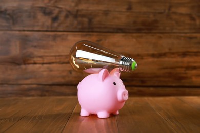 Photo of Piggy bank and light bulb on wooden table. Energy saving concept