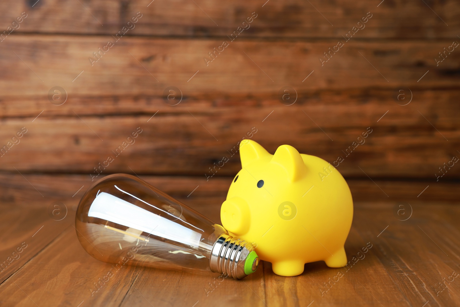 Photo of Piggy bank and light bulb on wooden table. Energy saving concept