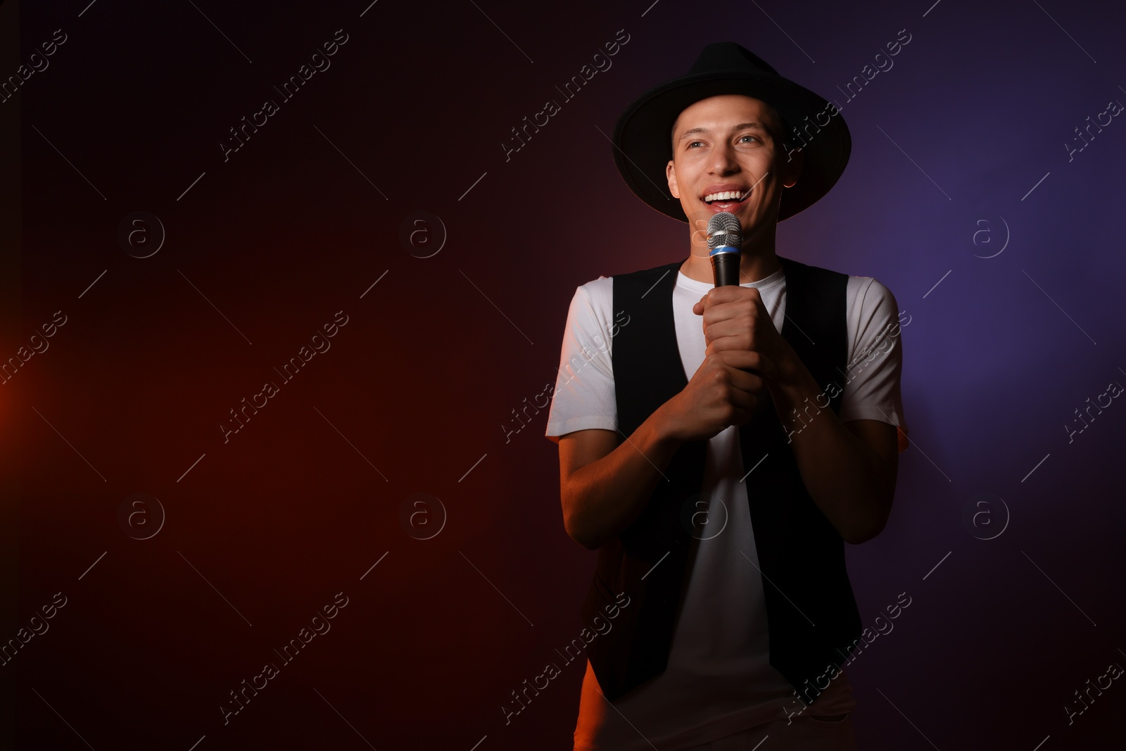 Photo of Talented young man singing on dark background with color light. Space for text