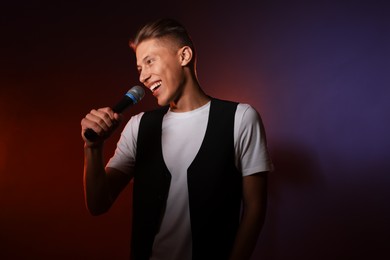 Photo of Talented young man singing on dark background with color light