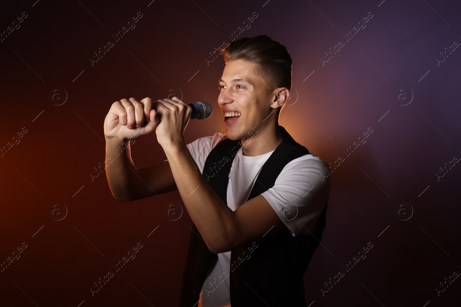 Photo of Talented young man singing on dark background with color light