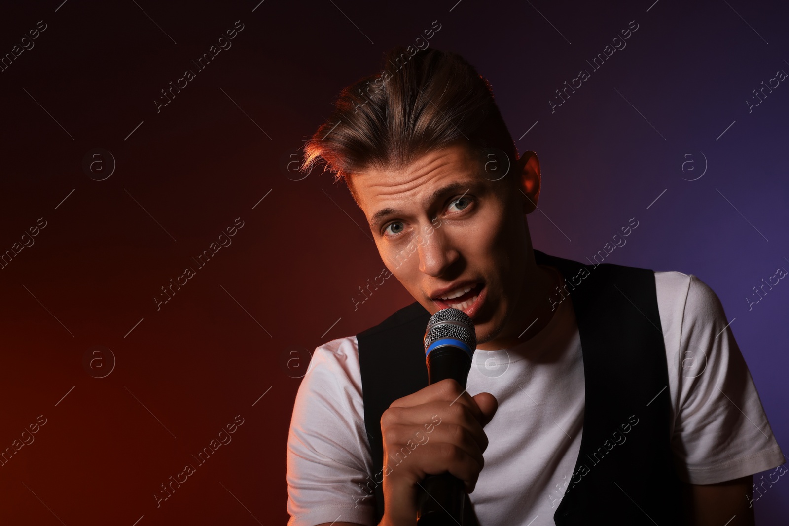 Photo of Talented young man singing on dark background with color light