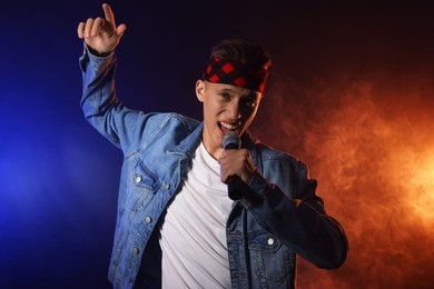 Photo of Talented singer performing on dark background with color lights and smoke