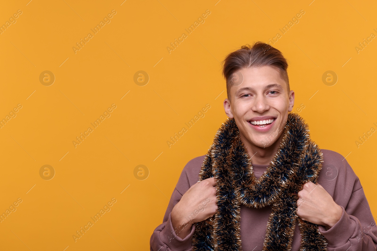 Photo of Happy young man with tinsel on orange background, space for text