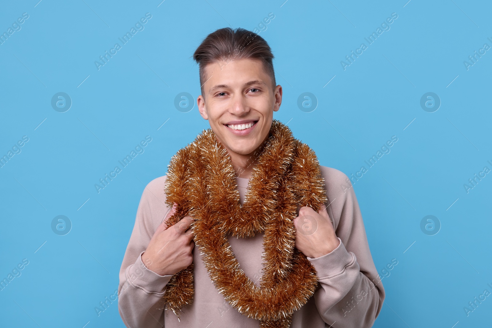 Photo of Happy young man with bright tinsel on light blue background