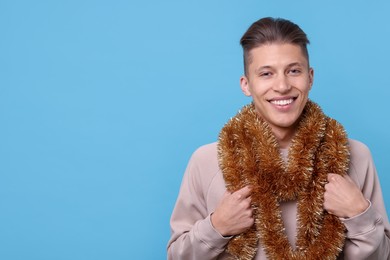 Photo of Happy young man with bright tinsel on light blue background, space for text