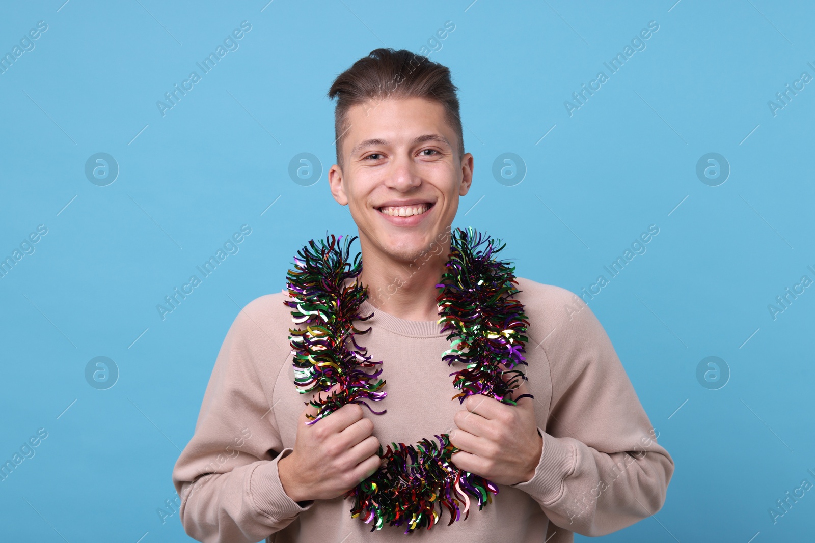 Photo of Happy young man with tinsel on light blue background