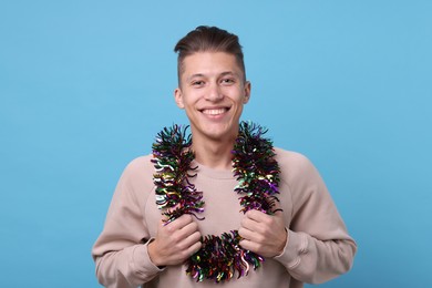 Photo of Happy young man with tinsel on light blue background