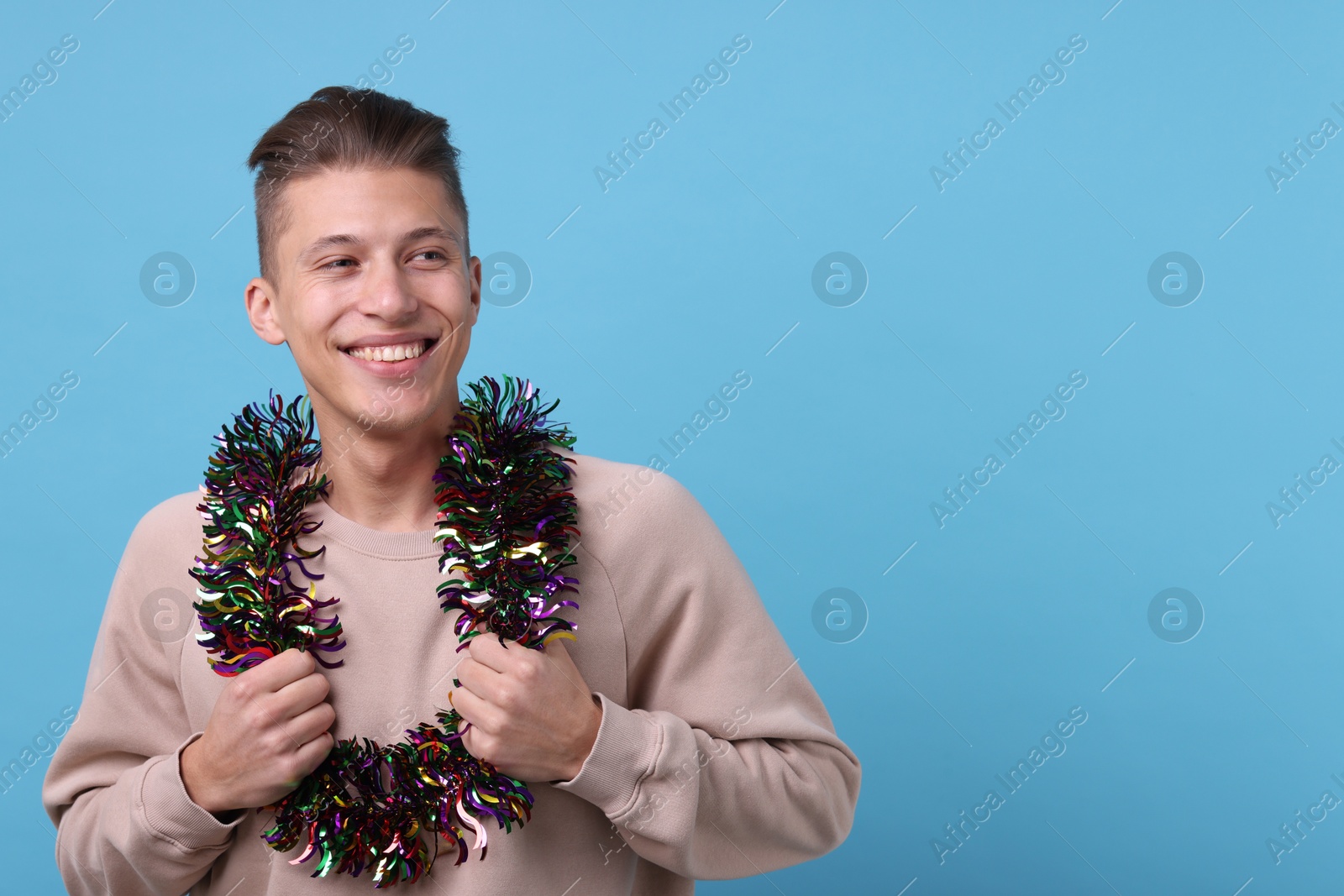 Photo of Happy young man with tinsel on light blue background, space for text