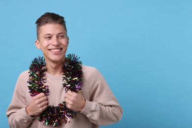 Photo of Happy young man with tinsel on light blue background, space for text