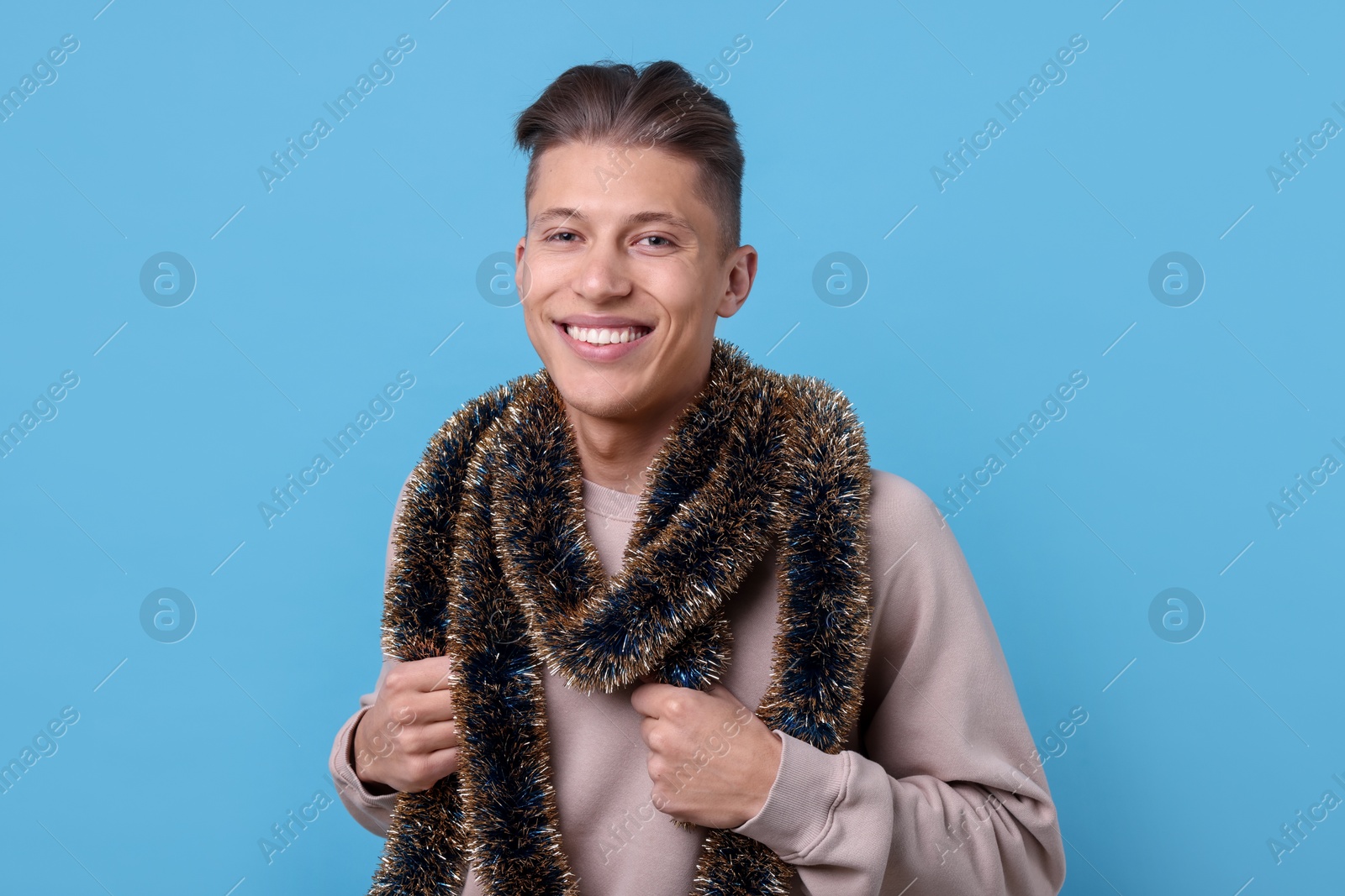 Photo of Happy young man with tinsel on light blue background