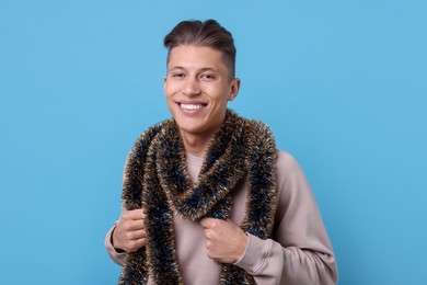 Photo of Happy young man with tinsel on light blue background