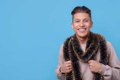 Photo of Happy young man with tinsel on light blue background, space for text