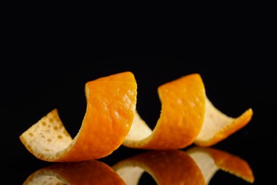 Photo of One curly orange peel on black mirror surface, closeup