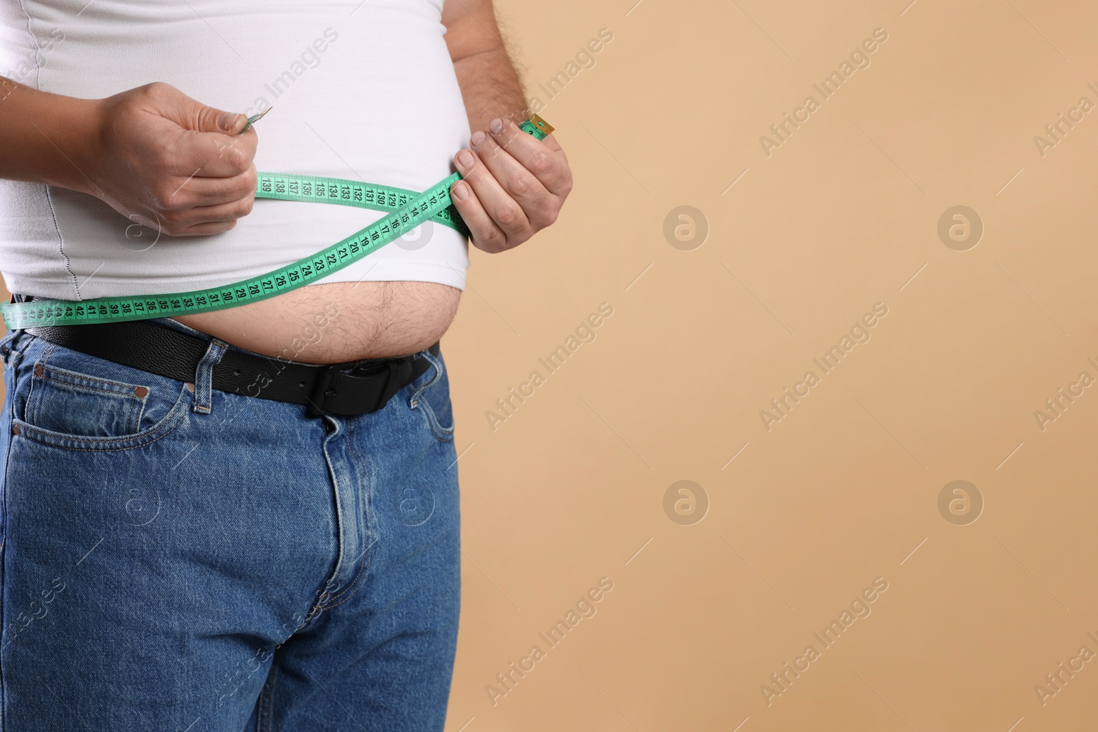 Photo of Overweight man measuring his belly with tape on beige background, closeup. Space for text