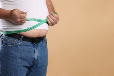 Photo of Overweight man measuring his belly with tape on beige background, closeup. Space for text