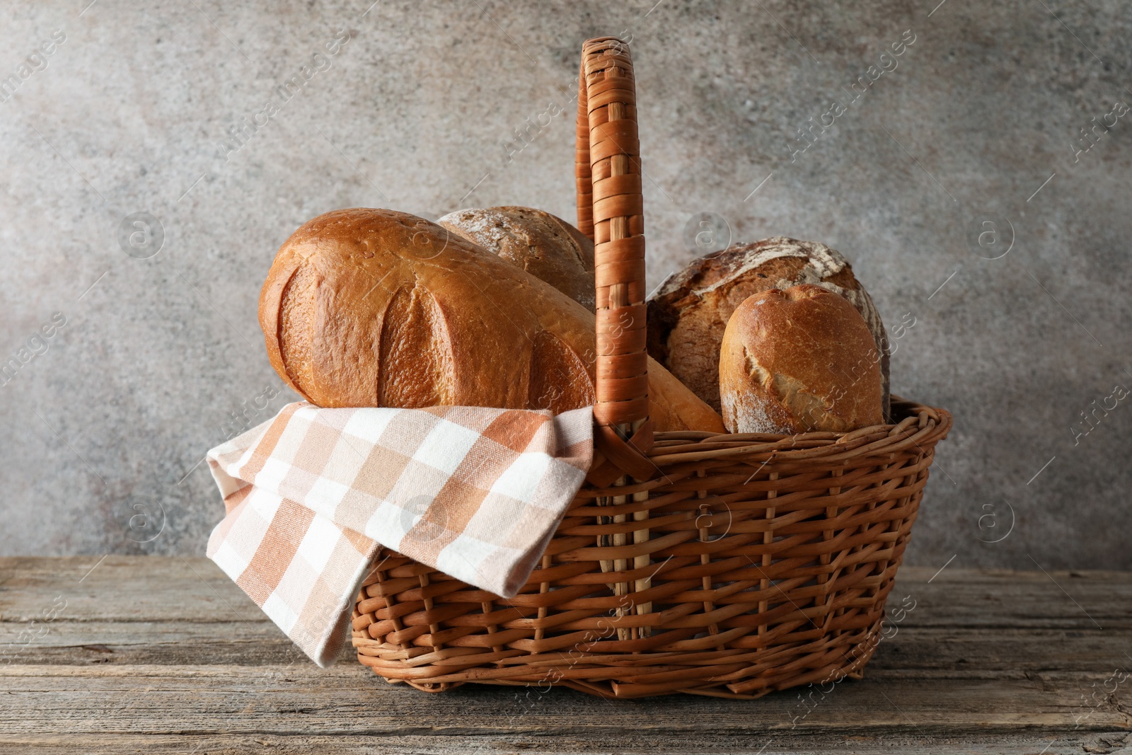 Photo of Different freshly baked bread loafs in wicker basket on wooden table