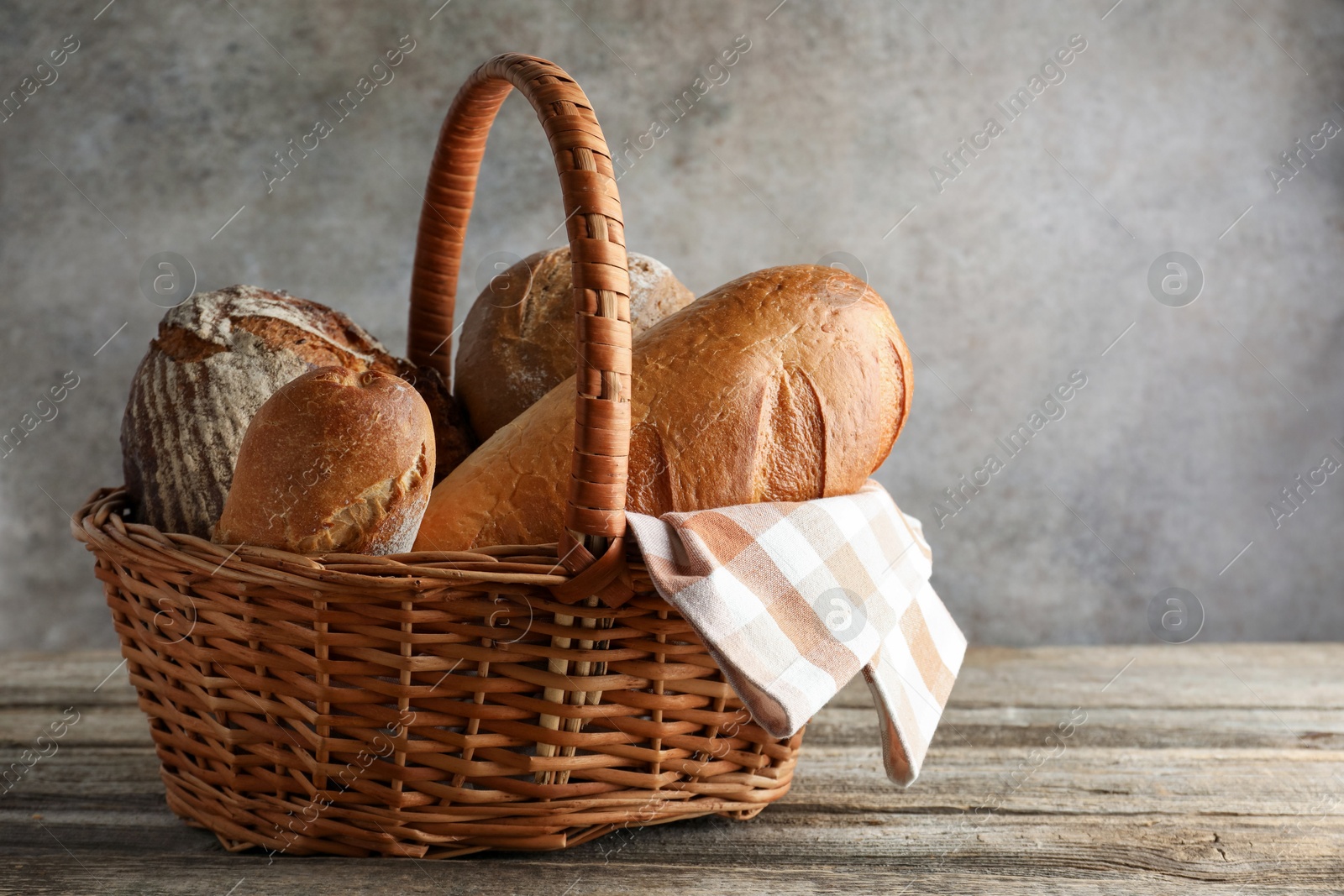 Photo of Different freshly baked bread loafs in wicker basket on wooden table, space for text