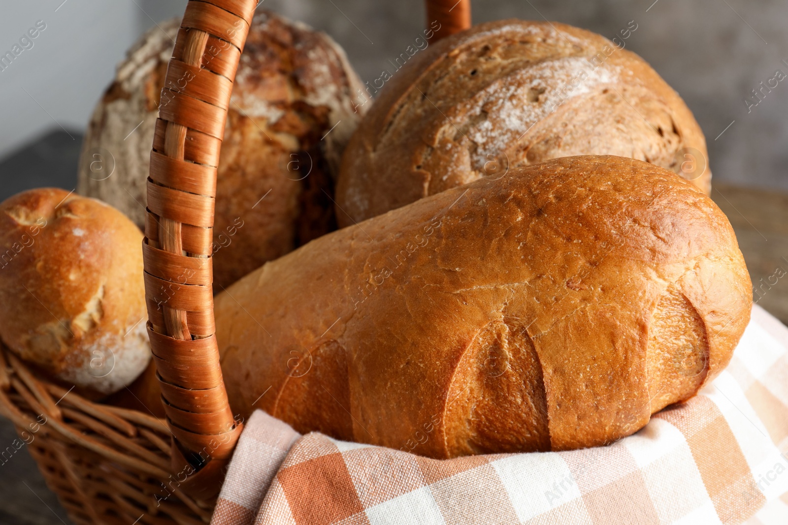 Photo of Different freshly baked bread loafs in wicker basket on table, closeup