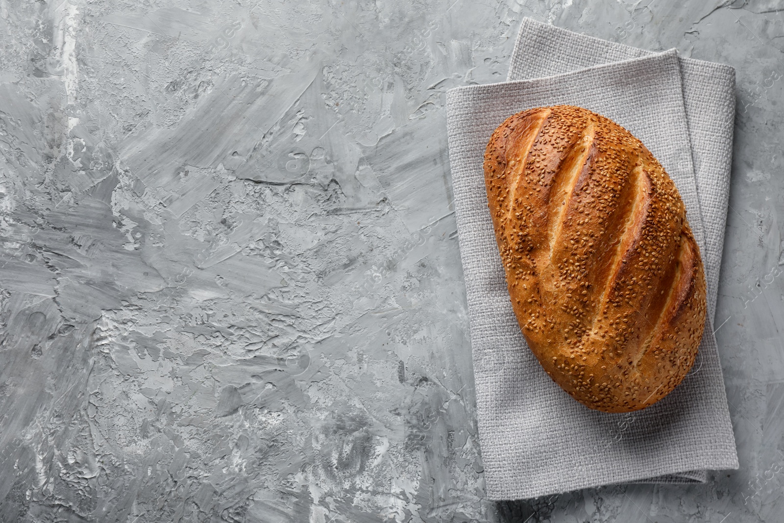 Photo of Freshly baked bread with seeds on grey table, top view. Space for text